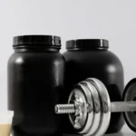 Potes de whey protein isolado ao lado de haltere e scoop de suplemento