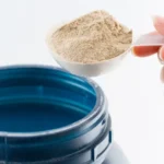 Colher medidora com pó de whey protein sendo retirada de um pote aberto