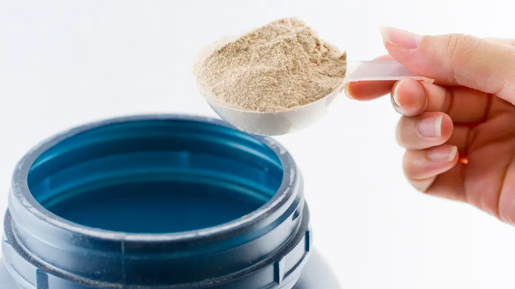 Colher medidora com pó de whey protein sendo retirada de um pote aberto